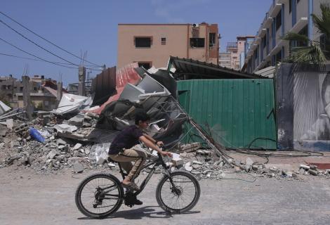 A boy rides his bike past buildings destroyed by airstrikes in Gaza