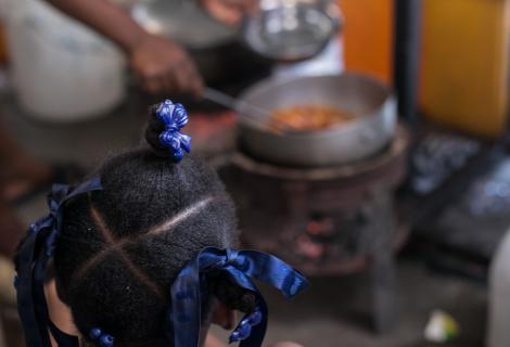 A young girl watches as a woman prepares food in a displacement camp in Haiti