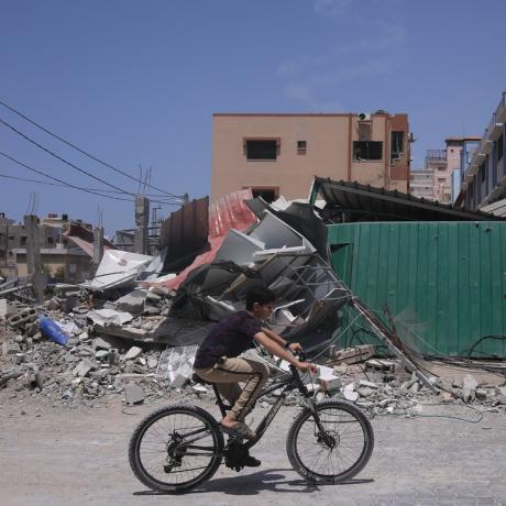 A boy rides his bike past buildings destroyed by airstrikes in Gaza